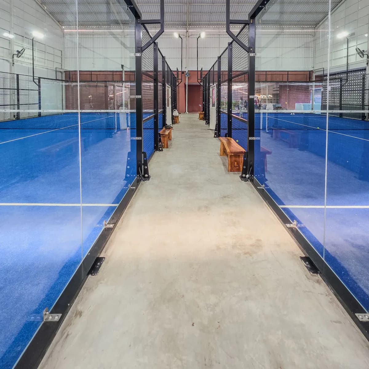 Row of indoor padel courts with blue turf seen from the walkway